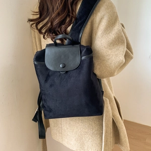 Rear view of a model wearing the black velvet backpack with leather flap and beige coat