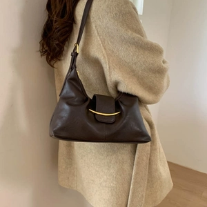 Detail shot of a dark brown hobo shoulder bag with a curved gold metal accent on the strap