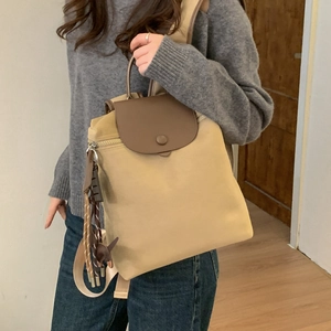 Side view of beige nylon backpack with brown leather flap on female model