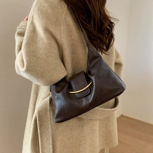 Close-up of a dark brown crescent bag with gold metal buckle worn on the shoulder
