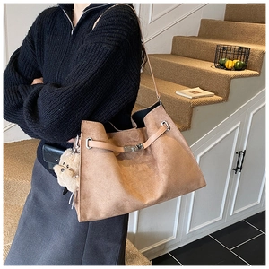 Detail of a brown suede tote bag with a gold metal turn-lock and a cute plush dog charm