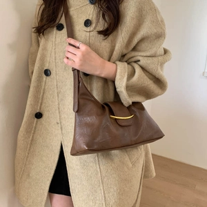 Detail of dark brown leather shoulder bag with gold metal trim on beige wool coat