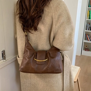 Detail of dark brown leather half-moon shoulder bag with gold hardware on a wool coat