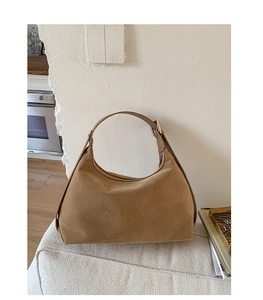 Detail of camel suede hobo bag with adjustable strap on a minimalist interior bench