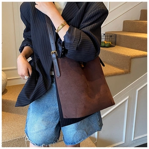 Detail of adjustable strap and gold buckle on a brown suede bucket bag worn with a blazer
