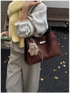 Detail of dark brown suede tote bag with metal twist lock and cute plush bear charm