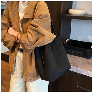 Lifestyle shot of black suede bucket bag worn by model in a minimalist home setting