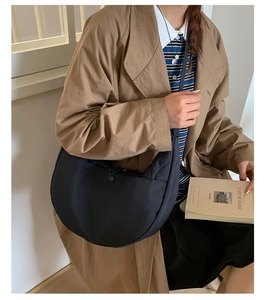 Dettaglio della borsa a mezzaluna nera in nylon indossata con un trench marrone chic