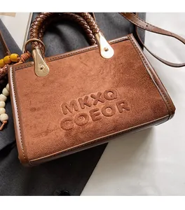 Gros plan du sac en daim marron avec logo embossé et poignée en cuir tressé