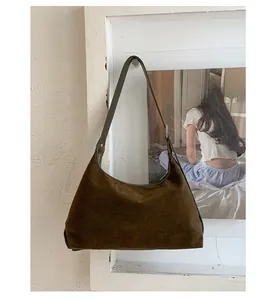 Detail of a vintage dark brown suede shoulder bag with thin straps against a white wall