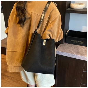 Detail of black suede bucket bag featuring a gold metal clasp and leather shoulder strap