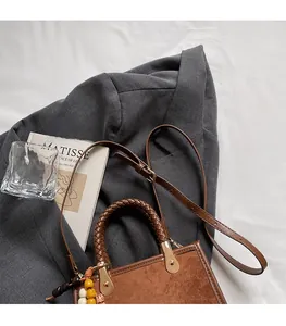 Détail d'un sac à main en daim marron avec poignée tressée et charm à perles