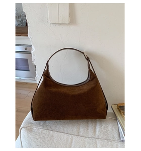 Close-up of a dark brown suede crescent handbag on a white chair in a home setting