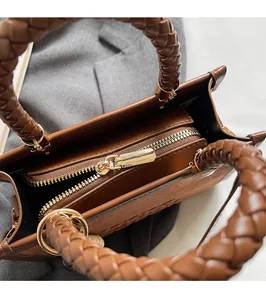 Détail d'un sac bandoulière en daim marron avec poignées tressées et fermeture éclair dorée