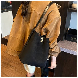 Detail of black faux suede bucket bag featuring a bright gold metal lock and leather strap
