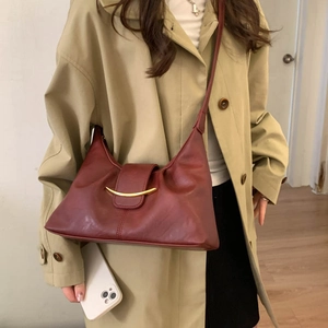 Detail of burgundy shoulder bag with golden crescent buckle on classic khaki trench coat