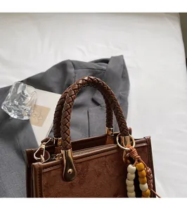 Détail de la poignée tressée et des ferrures d'un sac à main en daim marron