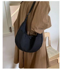 Dettaglio borsa a tracolla nera in nylon trapuntato indossata con un cappotto lungo marrone