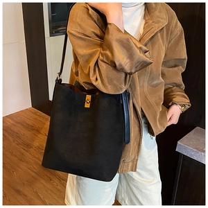 Detail of black suede bucket bag featuring a gold rectangular twist lock and leather strap