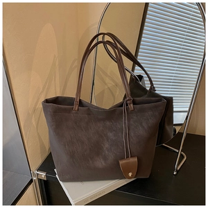 Detail of dark matte leather tote bag with thin shoulder straps and decorative pendant