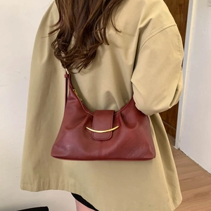 Close-up of burgundy leather dumpling bag with gold curved metal buckle on trench coat