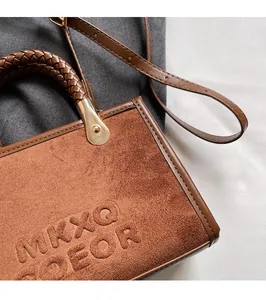 Détails d'un sac bandoulière en daim marron avec poignée tressée et logo gaufré