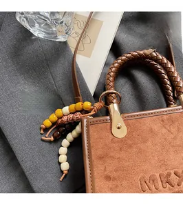 Détail d'un sac en daim marron avec poignée tressée et pendentif en perles colorées