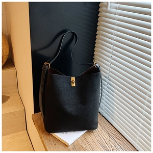 Detailed view of black suede bucket bag featuring golden buckle on a wooden desk