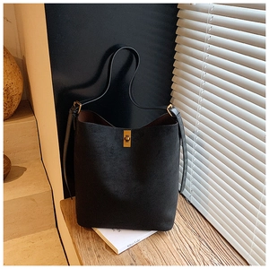Detail of black suede bucket bag featuring a premium gold twist lock and shoulder strap