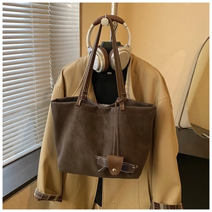 Detail of a brown suede tote bag with a leather glasses case charm in a cozy setting