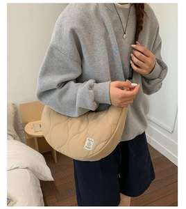 Dettaglio della borsa a mezzaluna trapuntata beige con cuciture a onda e logo