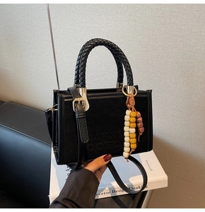 Détail d'un sac bandoulière noir en suédine avec poignée tressée et breloque perlée