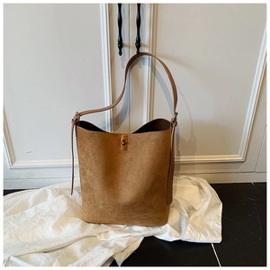 Detail of a brown suede bucket bag featuring a golden metal twist lock and minimalist texture
