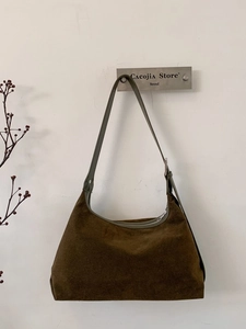 Minimalist brown suede hobo bag with adjustable strap hanging on a clean white wall