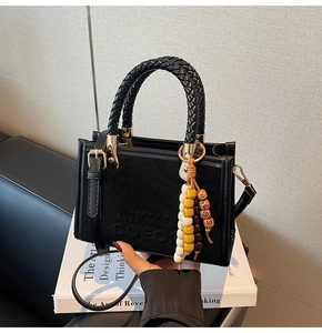 Détail du sac patchwork en daim noir avec poignées tressées et accessoire à pompons