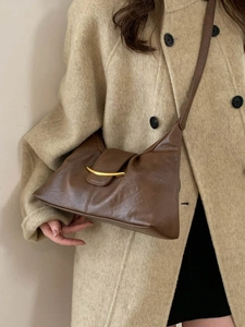 Dark brown leather dumpling shoulder bag with gold crescent moon metal buckle on beige coat