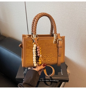 Détail du sac en daim avec poignées tressées, logo embossé et breloque en perles