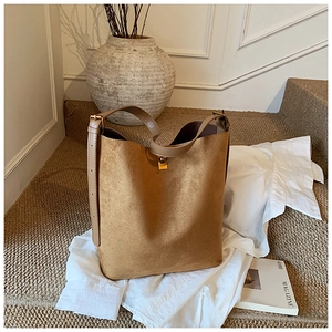 Detail of a brown suede bucket bag with smooth leather handles and golden metal buckle