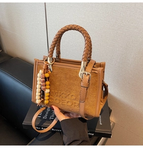 Détail du sac bandoulière en suède avec logo embossé, poignée tressée et perles en bois