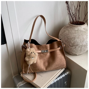 Detail of tan suede tote bag featuring metallic clasp and cute plush dog charm