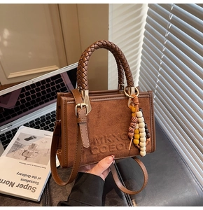 Sac bandoulière en daim marron avec poignée tressée et charm perlé dans un décor de bureau