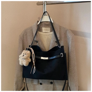 Detail of black tote bag with metal twist lock, decorative belt and plush bear charm