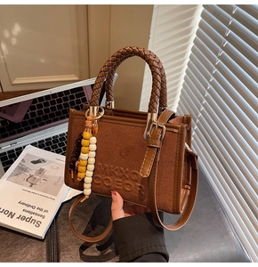 Détail du sac bandoulière en daim marron avec logo embossé et poignée en cuir tressé