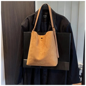 Detailed view of brown suede bucket bag featuring a golden turn-lock and adjustable strap