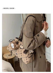 Model wearing a large cream tote bag with bear print and brown plush charm on shoulder
