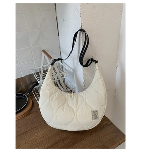 Dettaglio della borsa a mezzaluna trapuntata beige con tracolla e logo distintivo