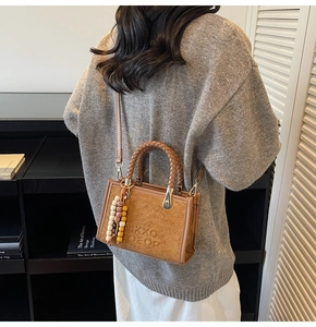 Sac bandoulière en daim marron avec anses tissées et breloque porté par mannequin