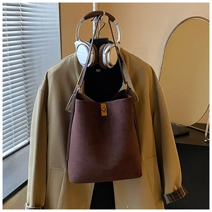 Detail of deep brown suede bucket bag with gold metallic twist-lock closure on a stand