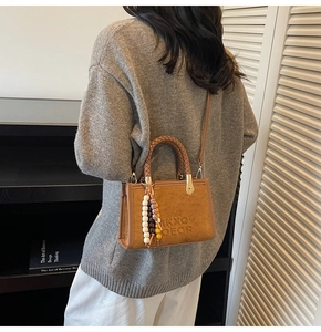 Détail d'un sac bandoulière vintage en daim marron avec poignée tressée et charm perlé
