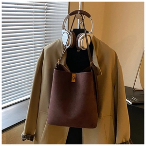 Close-up of brown suede bucket bag with gold rectangular clasp on a stylish hanger